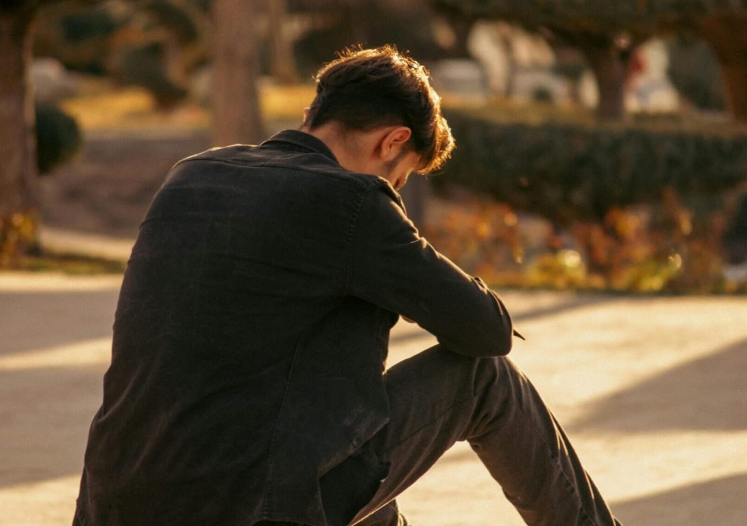 man sitting alone looking down thinking