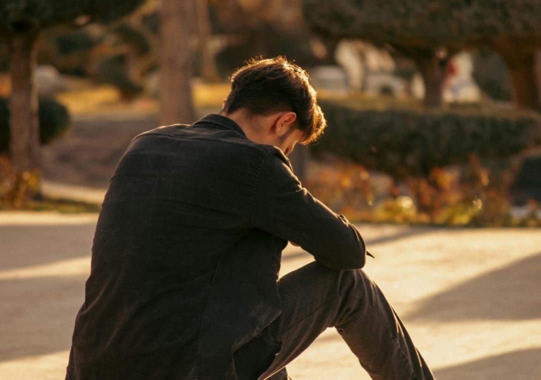 man sitting alone looking down thinking